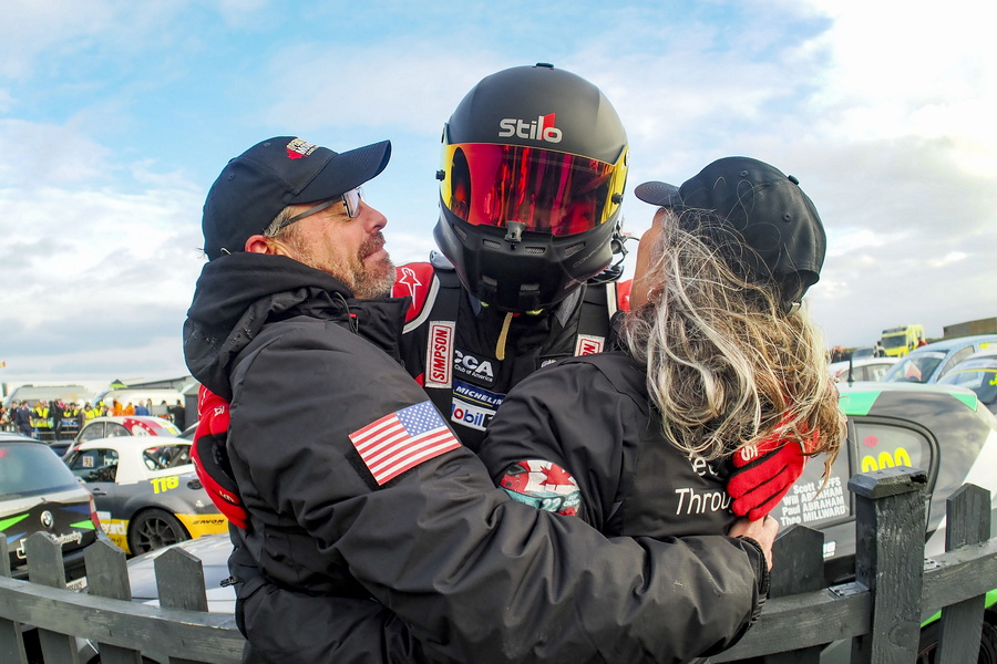 Race car driver hugging two people.