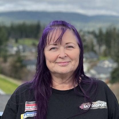 Woman with purple hair smiling outdoors.