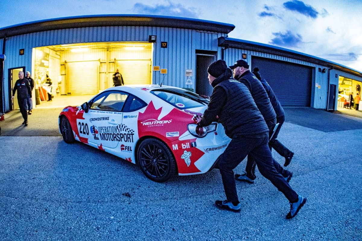 Three men pushing a white race car.