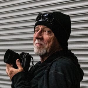 Older man holding camera, smiling.