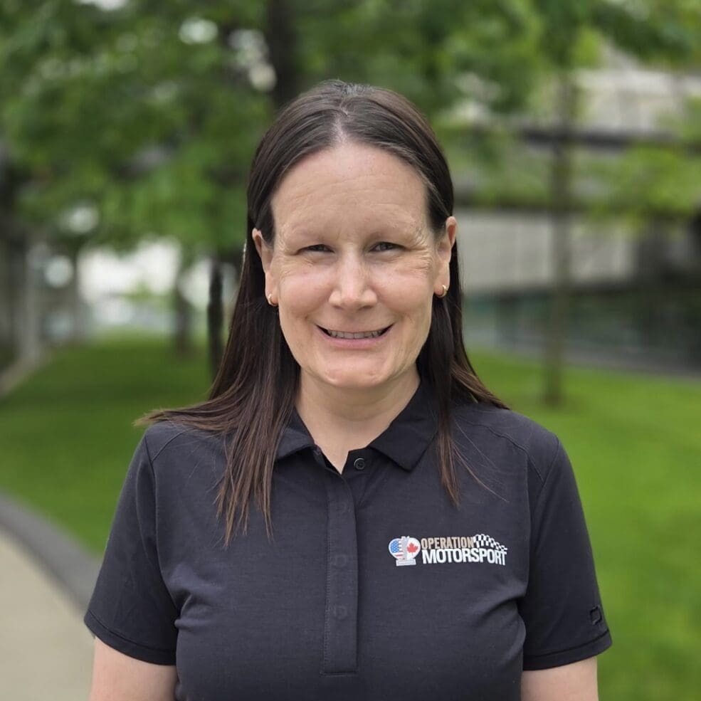Smiling woman outdoors wearing a black polo shirt with a logo.