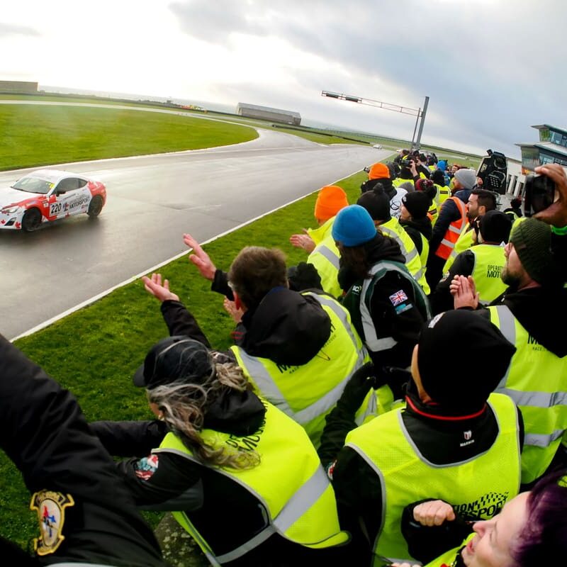 Race car driving past cheering fans.