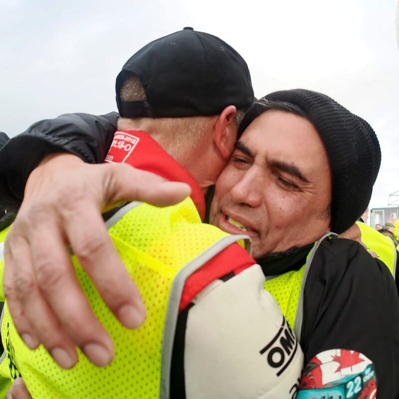 Two men in racing gear embrace.